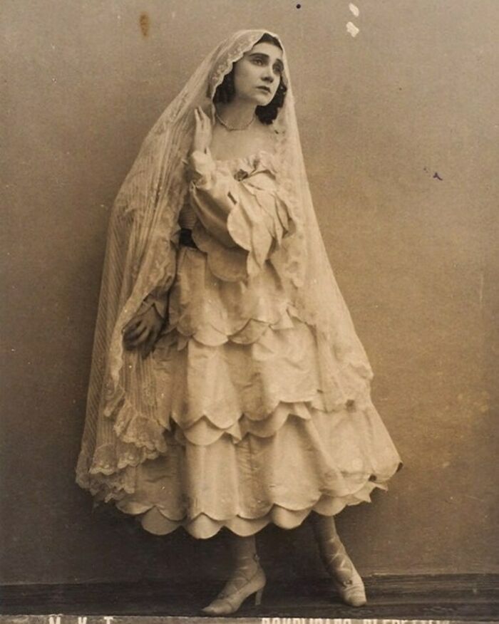 Victorian era woman in layered dress and veil posing with a thoughtful expression in a vintage black and white photo.