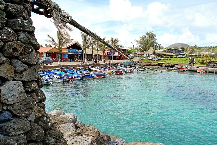 Colorful boats docked at a pier in a remote location with clear turquoise water and palm trees along the shore.