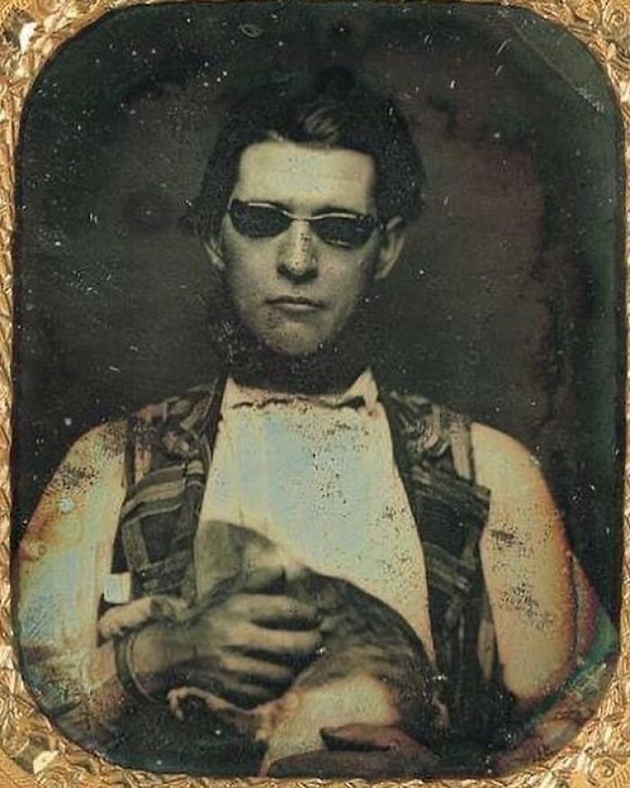 Victorian era weird photo of a man wearing dark glasses holding a cat, showing the unusual side of the time period.