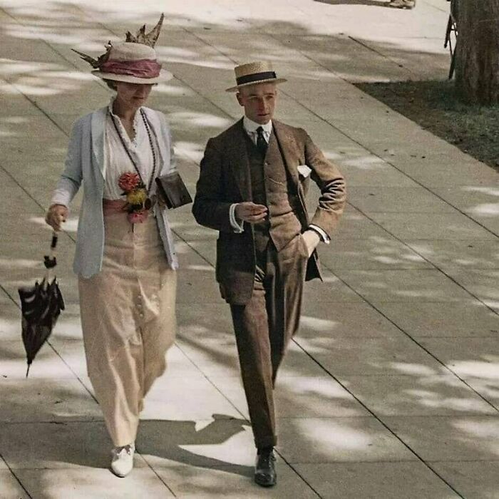 Victorian era woman with umbrella and man in suit wearing hat walking on sunny sidewalk from weird photos.