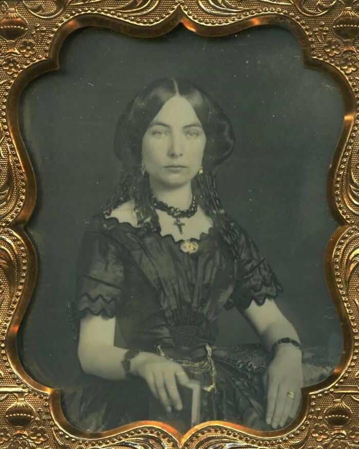 Victorian era woman in dark dress with antique jewelry sitting for a formal 19th-century portrait photograph.