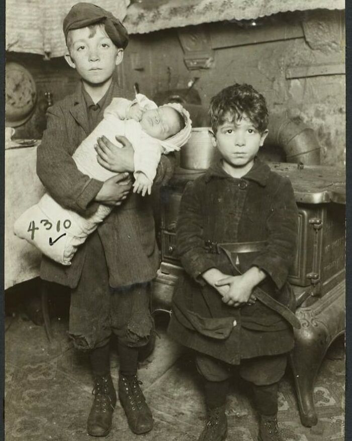 Victorian era photo showing two boys in worn clothing, one holding a baby, illustrating childhood in a different time.