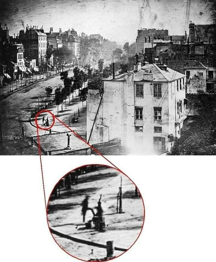 Black and white Victorian era photo showing a city street with an eerie figure circled and zoomed in.
