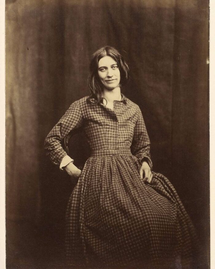 Victorian era weird photo of a woman in a checkered dress sitting with hands behind her back, showing unusual posture.