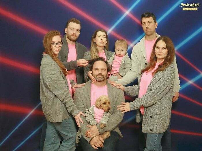Group photo of seven people and a dog in matching pink shirts and gray cardigans, an awkward studio pic with laser lights.