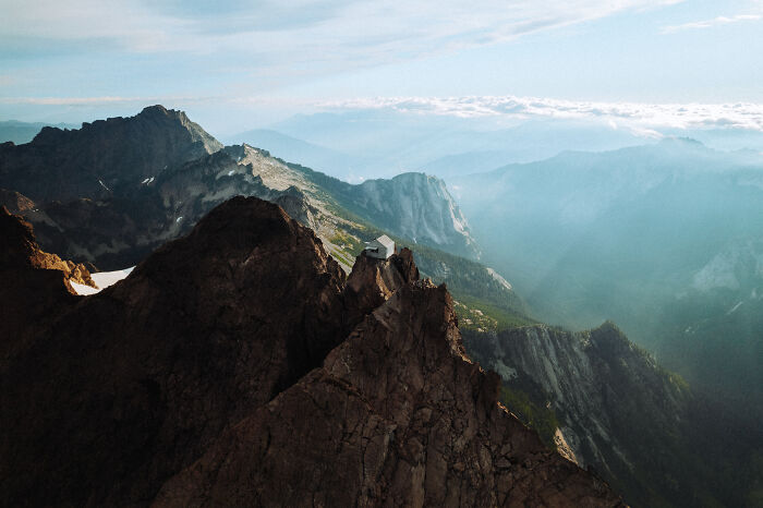 Mountain peak with a small cabin surrounded by vast landscape, reflecting a journey to find direction and purpose. Mountain peak with a small cabin surrounded by vast landscape, reflecting a journey to find direction and purpose.