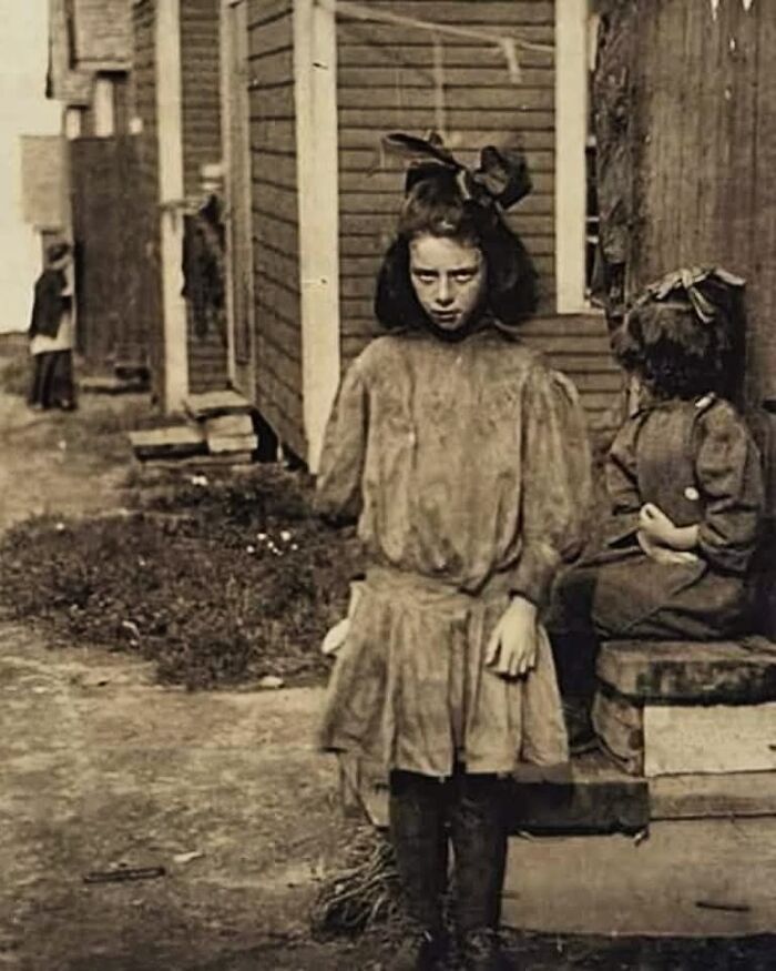 Victorian era weird photo showing a young girl in old-fashioned clothing standing in an alley near a building.