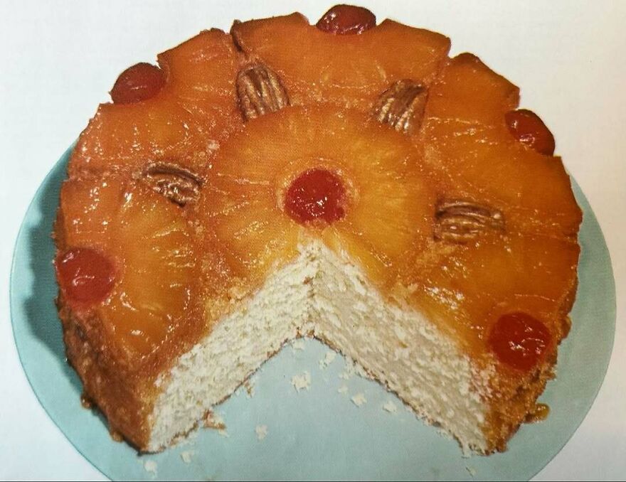 Vintage pineapple upside-down cake with cherries and pecans on a blue plate, showcasing interesting vintage recipes.