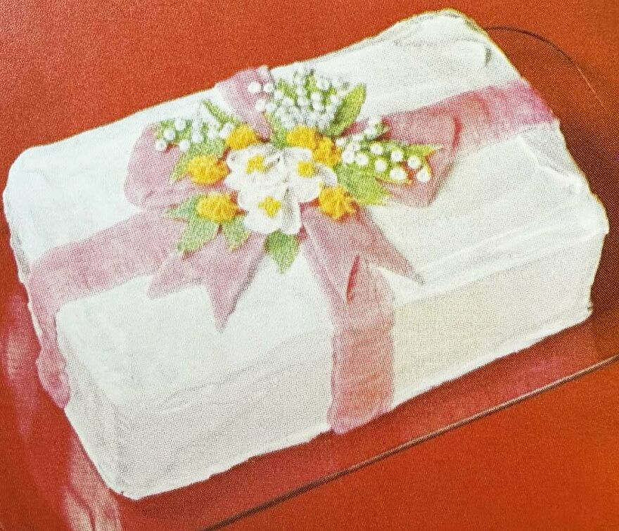 Vintage recipe cake decorated with frosting flowers and a large pink bow, showcasing interesting vintage recipes and past dishes.