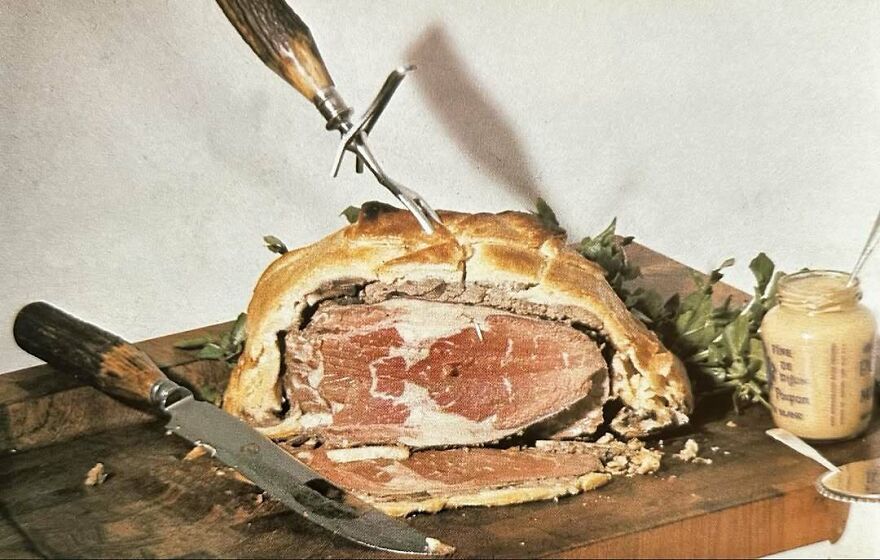 Vintage recipe featuring a bizarre meat dish wrapped in pastry with a carving fork and knife on a wooden board.