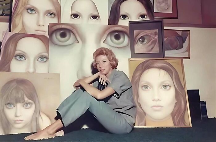 Woman artist sitting among large portrait paintings of women with striking eyes, highlighting overlooked women in history achievements.