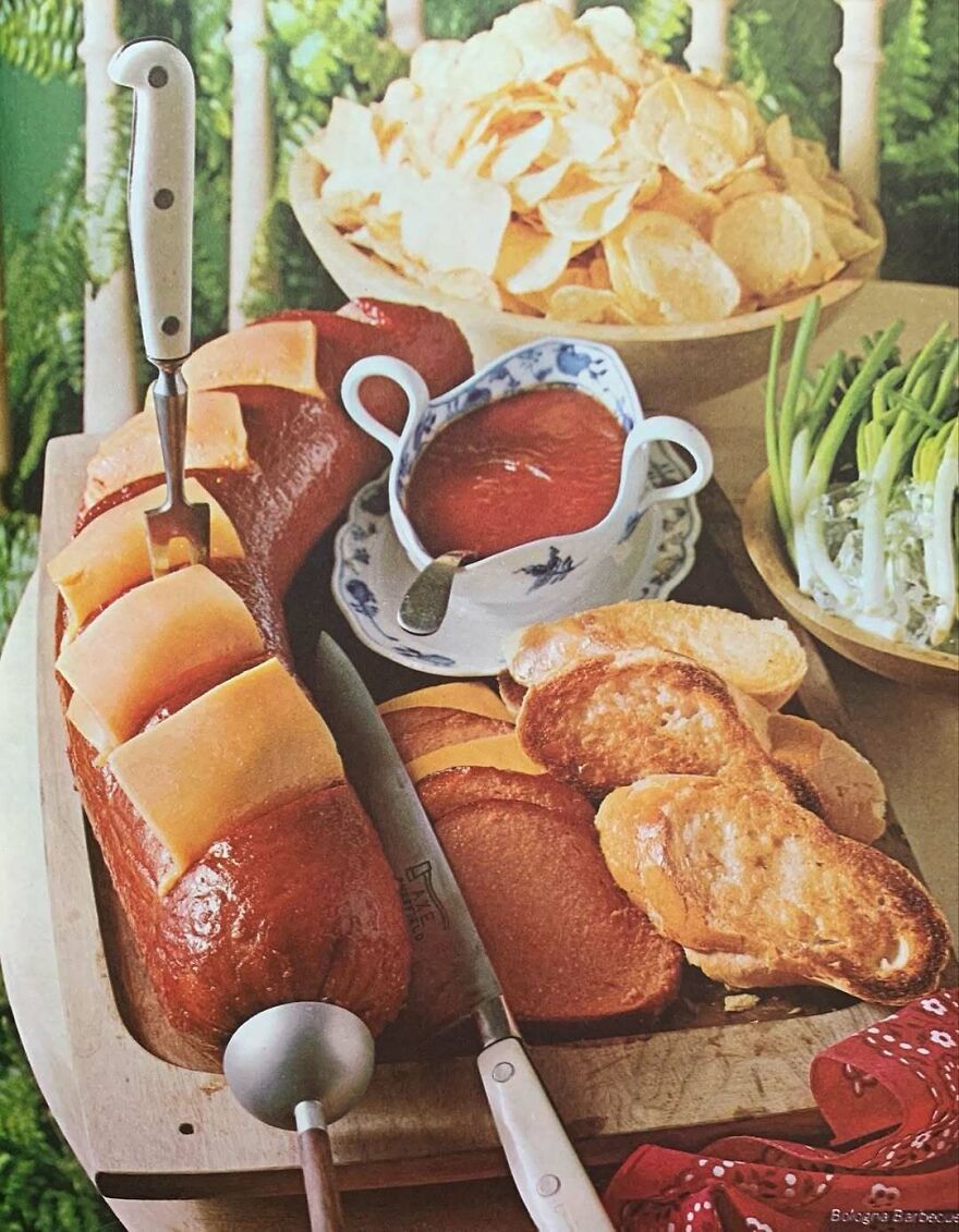 Vintage recipes featuring a large sausage with cheese, ketchup, toasted bread, chips, and green onions on a wooden tray.