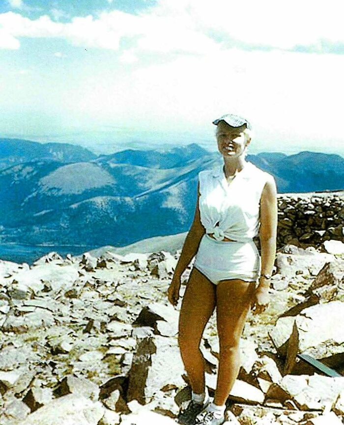 Woman standing on rocky mountain peak with vast landscape in background, representing overlooked women in history achievements.