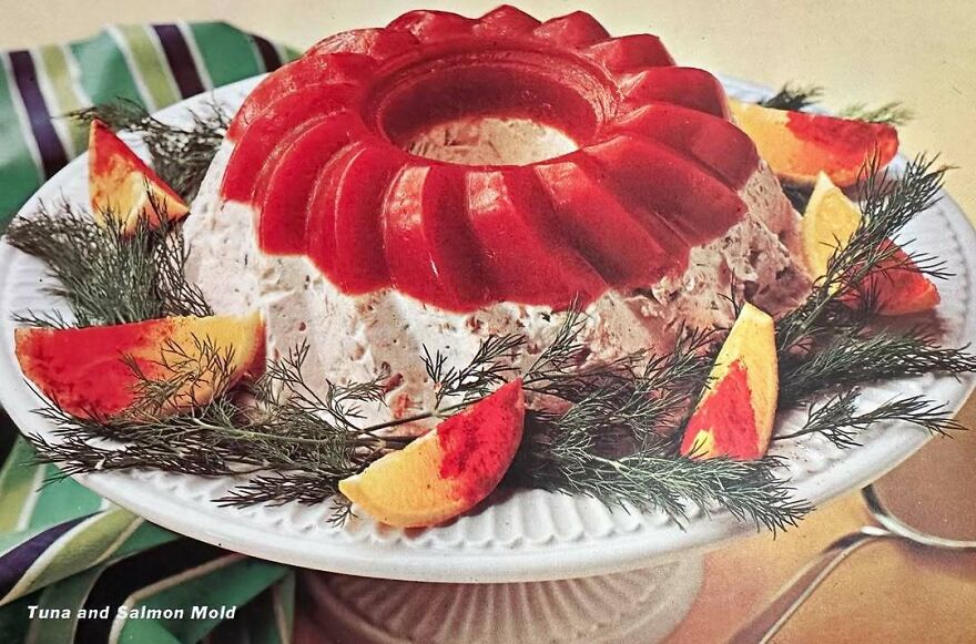 Vintage recipe of a tuna and salmon mold garnished with citrus slices and dill on a white serving plate.