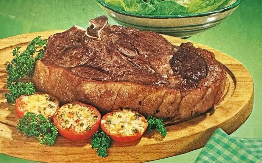 Vintage recipe showing a bizarre cooked meat dish served with stuffed tomatoes and garnished with fresh herbs on a wooden board.