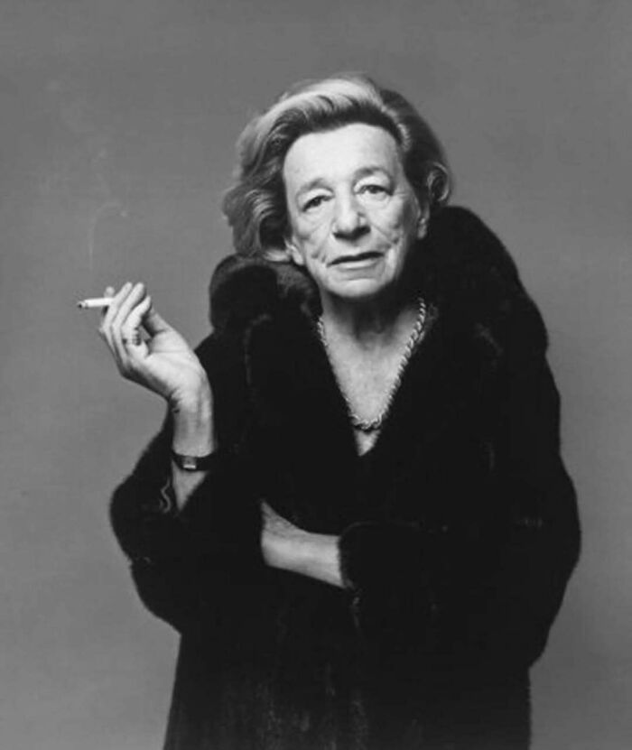 Black and white portrait of an older woman in a fur coat smoking a cigarette representing overlooked women in history.