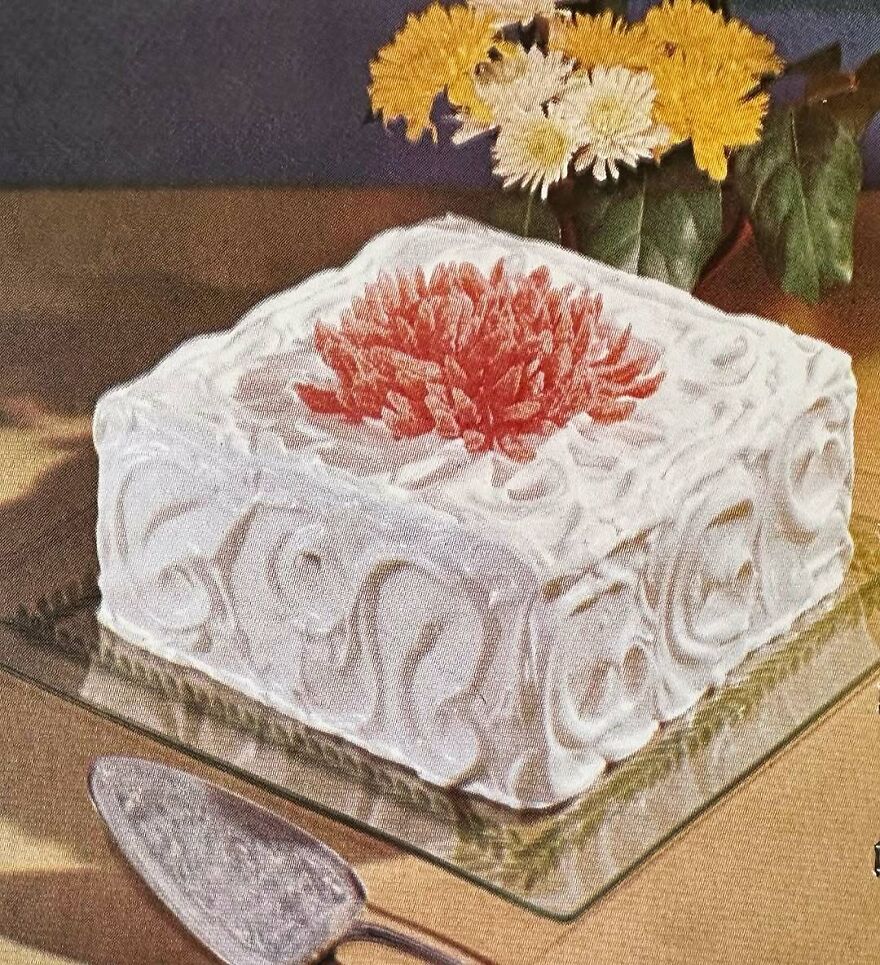 Square vintage cake with intricate white frosting and a red floral decoration, showcasing unique vintage recipes.