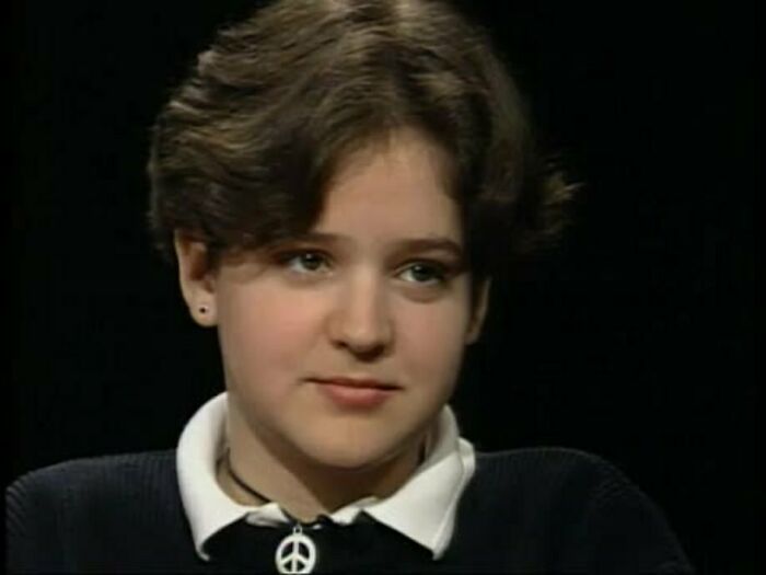 Young woman with short hair wearing a peace symbol necklace, representing overlooked women in history and their important achievements.