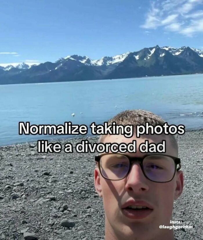 Young man wearing glasses by a lake with mountains, meme text about taking photos like a divorced dad, laughgorithm humor.