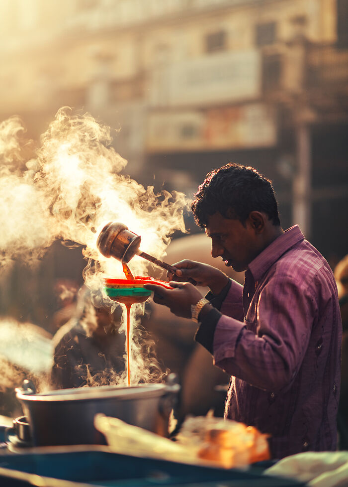 Street photography showing a man pouring steaming hot tea at a busy outdoor market in warm sunlight.