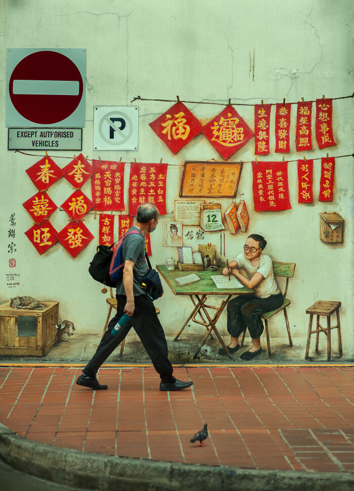 Man walking past colorful mural with Chinese calligraphy and street photography elements captured in urban setting.