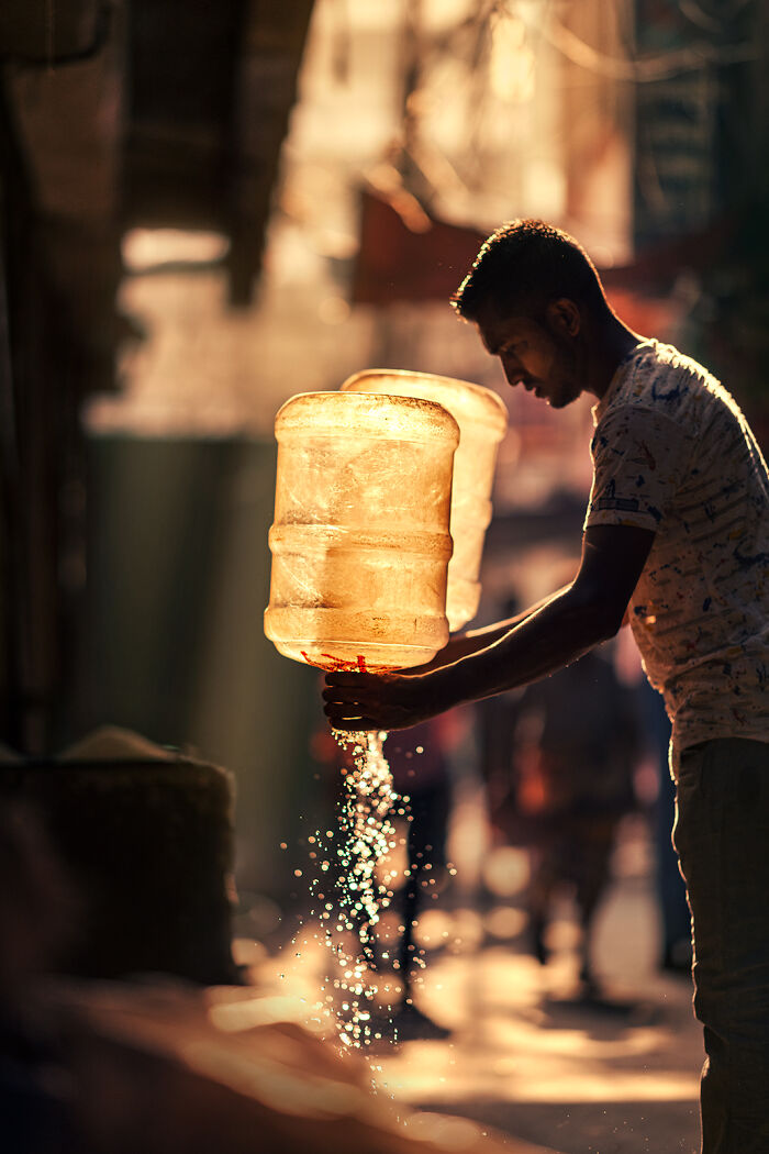 Man pouring water from large container on busy street in warm light, showcasing street photography around the world.