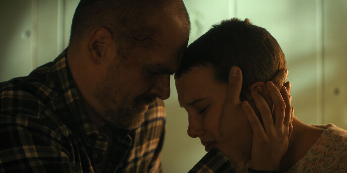 Millie Bobby Brown and David Harbour share an emotional moment in a dimly lit scene reflecting their complex relationship.