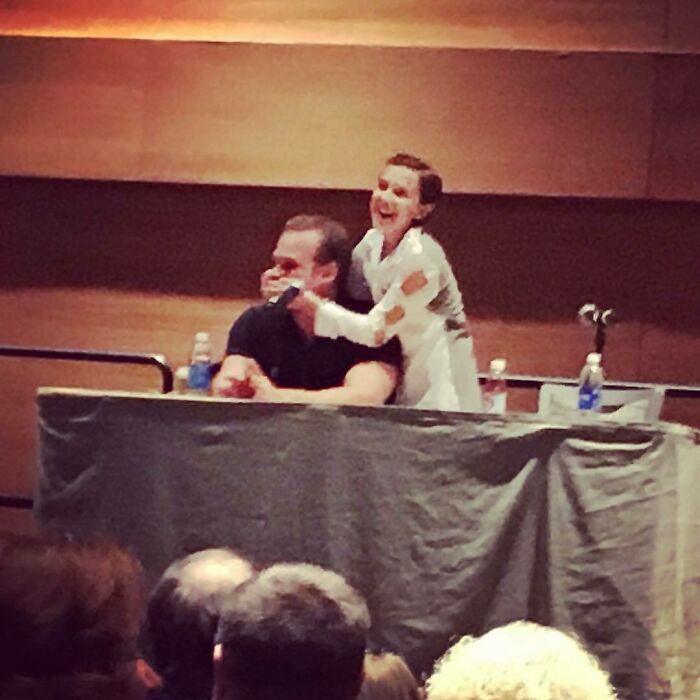Millie Bobby Brown and David Harbour sharing a joyful moment on stage during a public event discussing their relationship.