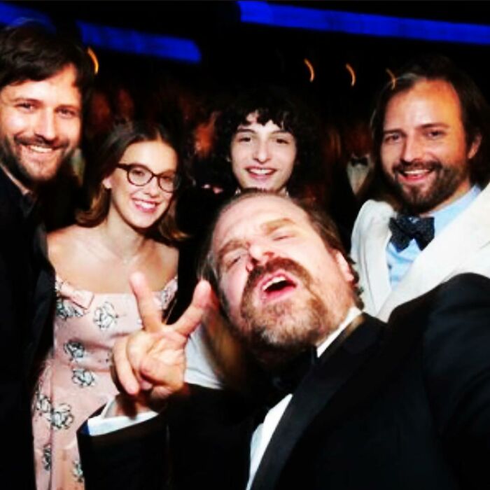 Millie Bobby Brown and David Harbour smiling with friends at an event highlighting their complex relationship amid allegations