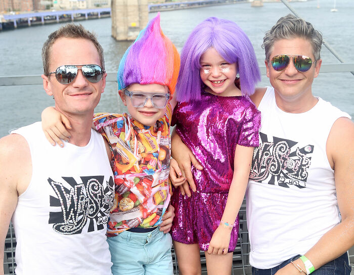 Neil Patrick Harris' daughter Harper in a vibrant purple outfit and wig, smiling with family by a waterfront. Neil Patrick Harris' daughter Harper in a vibrant purple outfit and wig, smiling with family by a waterfront.