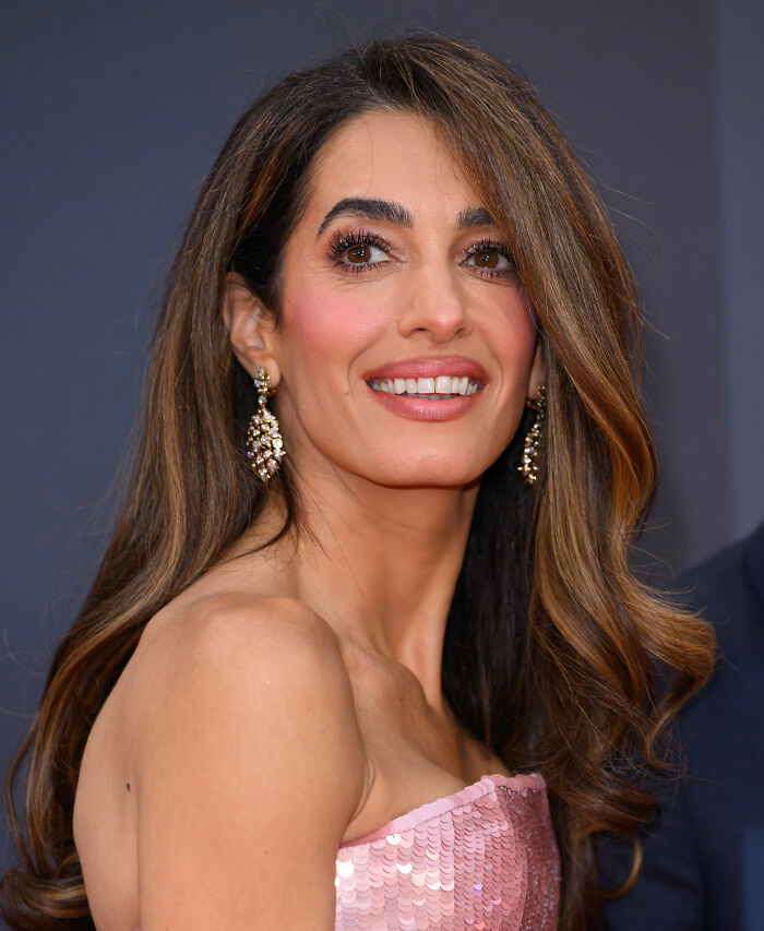 Amal Clooney smiling at an event, wearing elegant earrings and a pink sequined strapless dress, Photoshop blunder discussed.