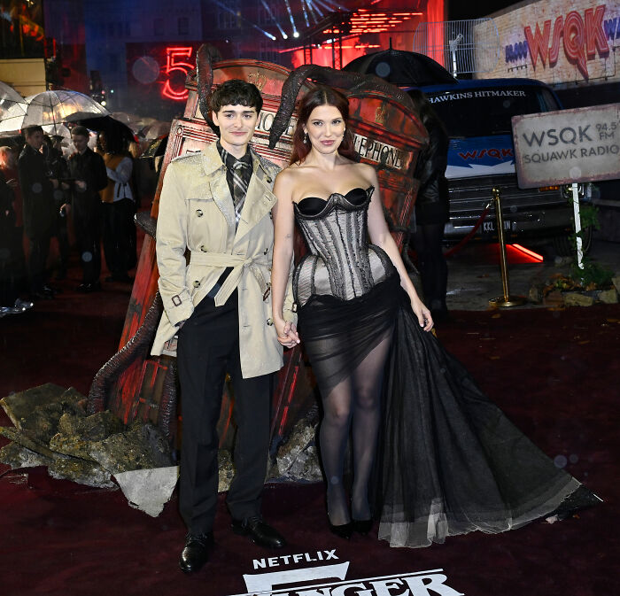 Millie Bobby Brown wearing lingerie with a train and a sheer black skirt on Stranger Things red carpet event.