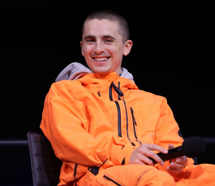 Timothée Chalamet smiling in bright orange jacket during a panel, reflecting on going into psychosis moments.