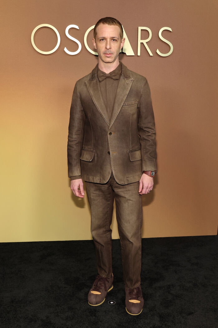 Man in a brown suit with bow tie and unusual shoes at a red carpet event, highlighting fashion disasters at Governors Awards.