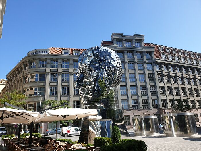 Reflective metal sculpture of a human head in a city square, showcasing spectacular sculptures across the globe.