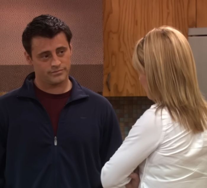 Matt LeBlanc as Joey wearing a navy jacket, speaking with a blonde woman in a kitchen setting during unaired episodes.