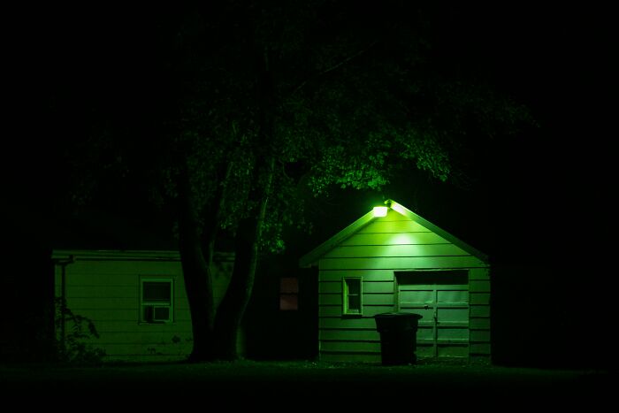 Small house and garage illuminated by green outdoor light at night, reflecting themes of family conflict and loss after mom’s passing.