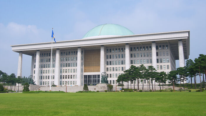 South Korean government building with green lawn under blue sky, related to world’s smartest man seeking US asylum news. South Korean government building with green lawn under blue sky, related to world’s smartest man seeking US asylum news.