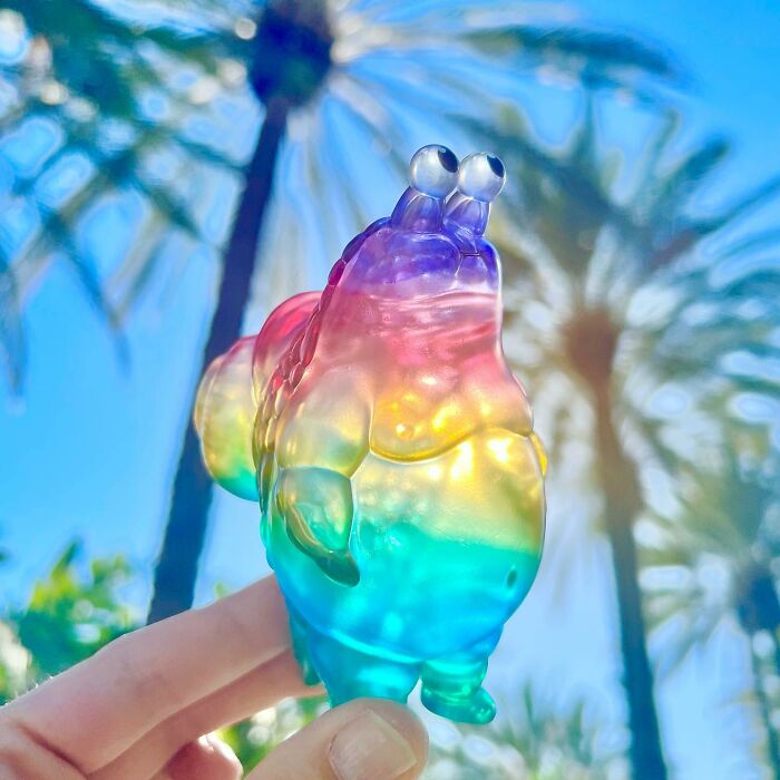 Colorful quirky sculpture held up against a blue sky with palm trees, showcasing vibrant personality and artistic design.