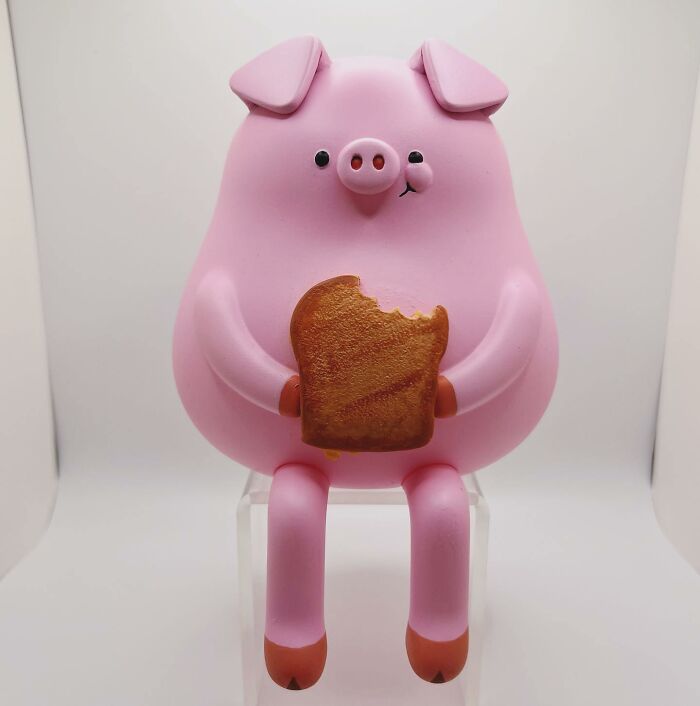 Pink quirky sculpture of a pig holding a bitten piece of bread, showcasing unique artistic personality and charm.