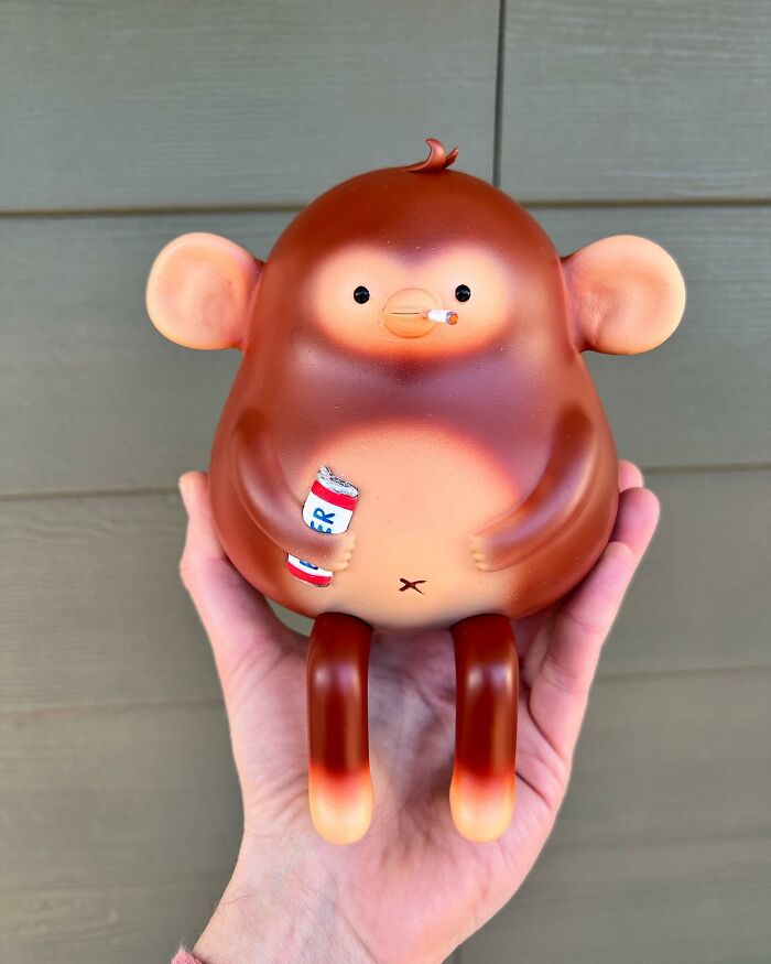 Hand holding a quirky sculpture of a monkey with cigarette and beer can, showcasing artist made personality-filled art.
