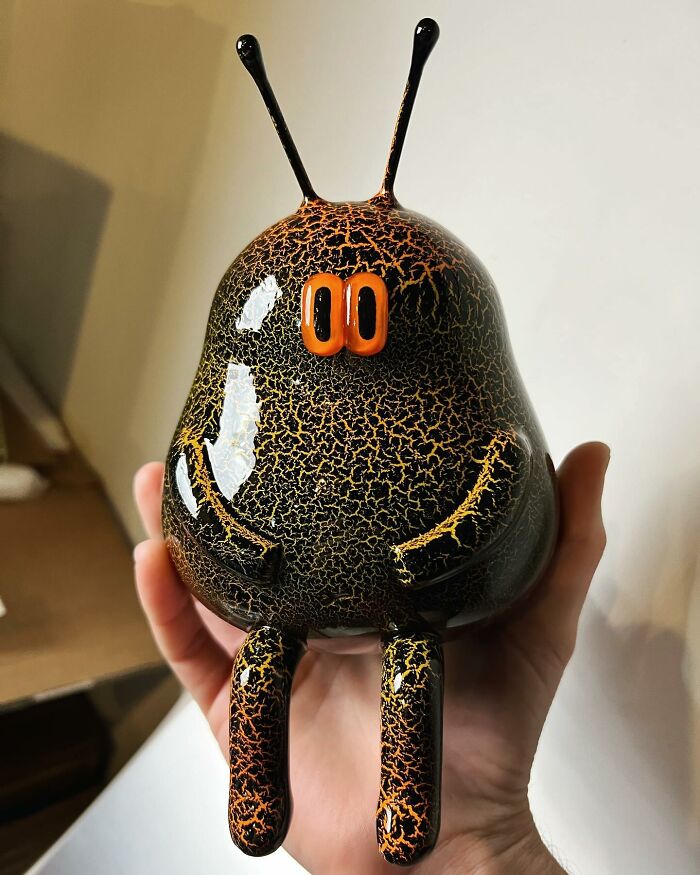 Glossy quirky sculpture with antennae and bright eyes held in hand, showcasing unique personality and artistic design.