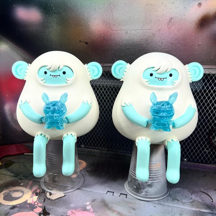 Two quirky sculptures with playful blue and white designs holding small blue figures, showcasing personality and artistic creativity.