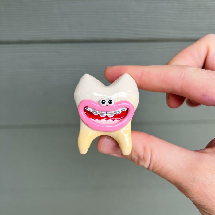 Hand holding a quirky sculpture of a tooth with eyes and a big smiling mouth, showing unique artistic personality.