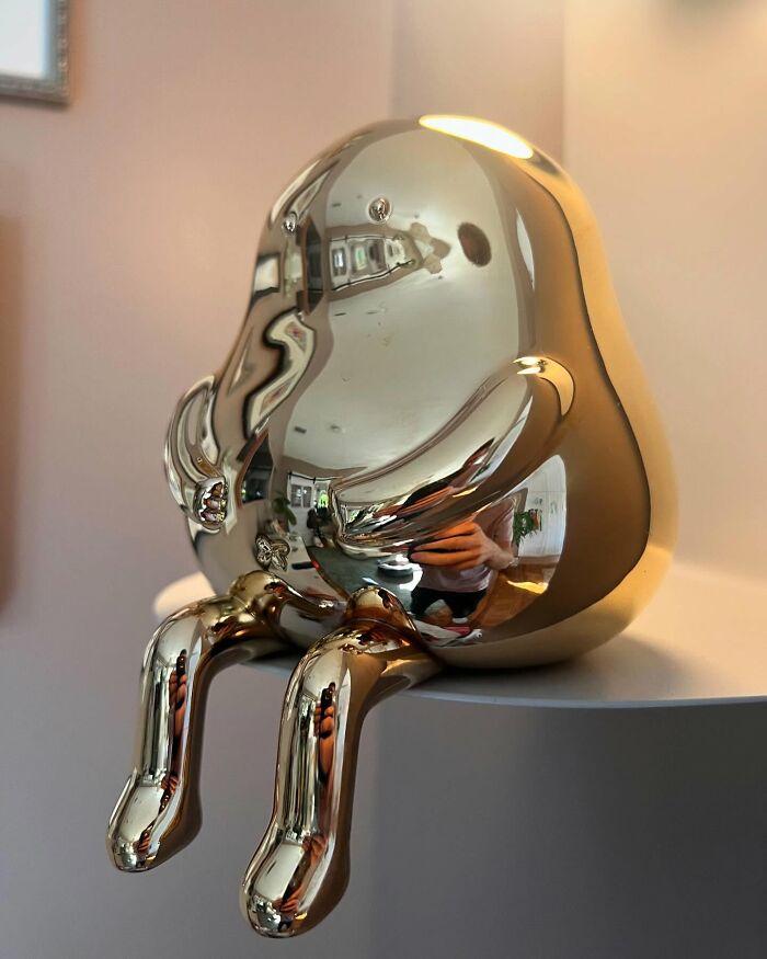 Glossy quirky sculpture with shiny reflective surface and playful rounded form sitting on a white table, showing personality.