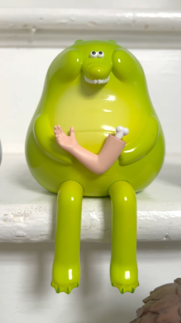 Bright green quirky sculpture with cartoonish face and a detached arm holding a bone, bursting with personality.