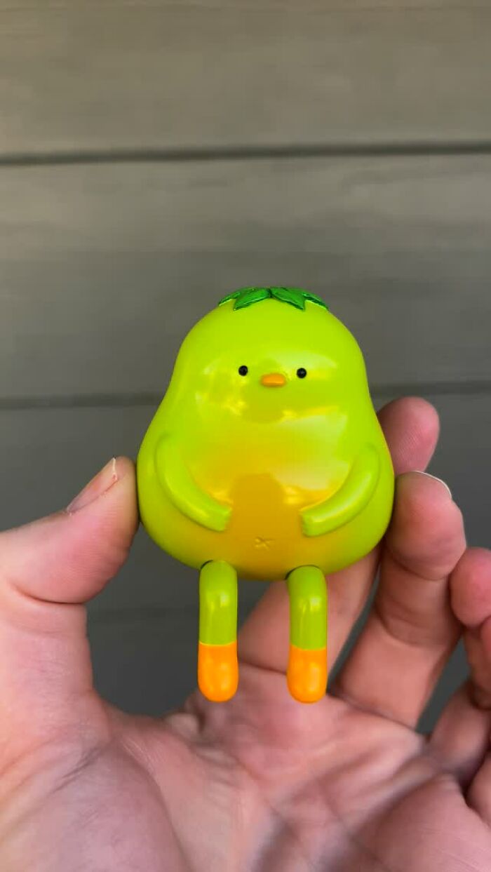 Hand holding a quirky small green sculpture with orange feet and leaf details, showcasing unique personality and charm.