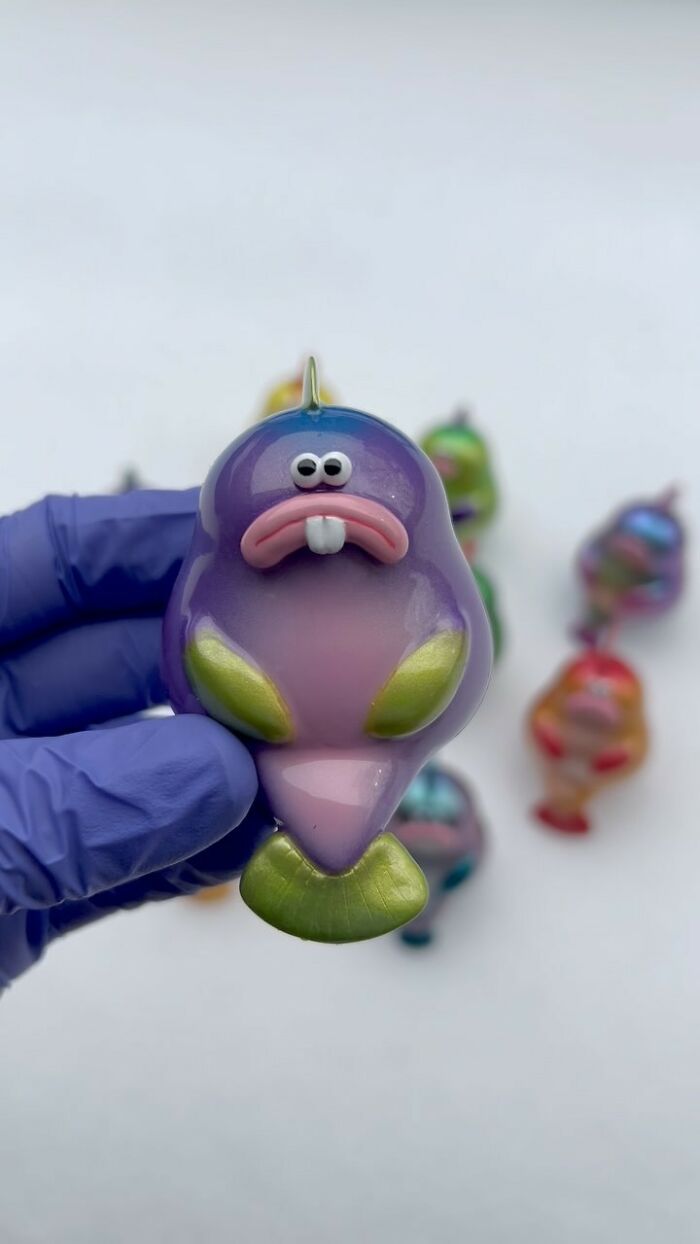 Purple quirky sculpture with cartoonish face held by gloved hand, one of 50 artist-made sculptures bursting with personality.