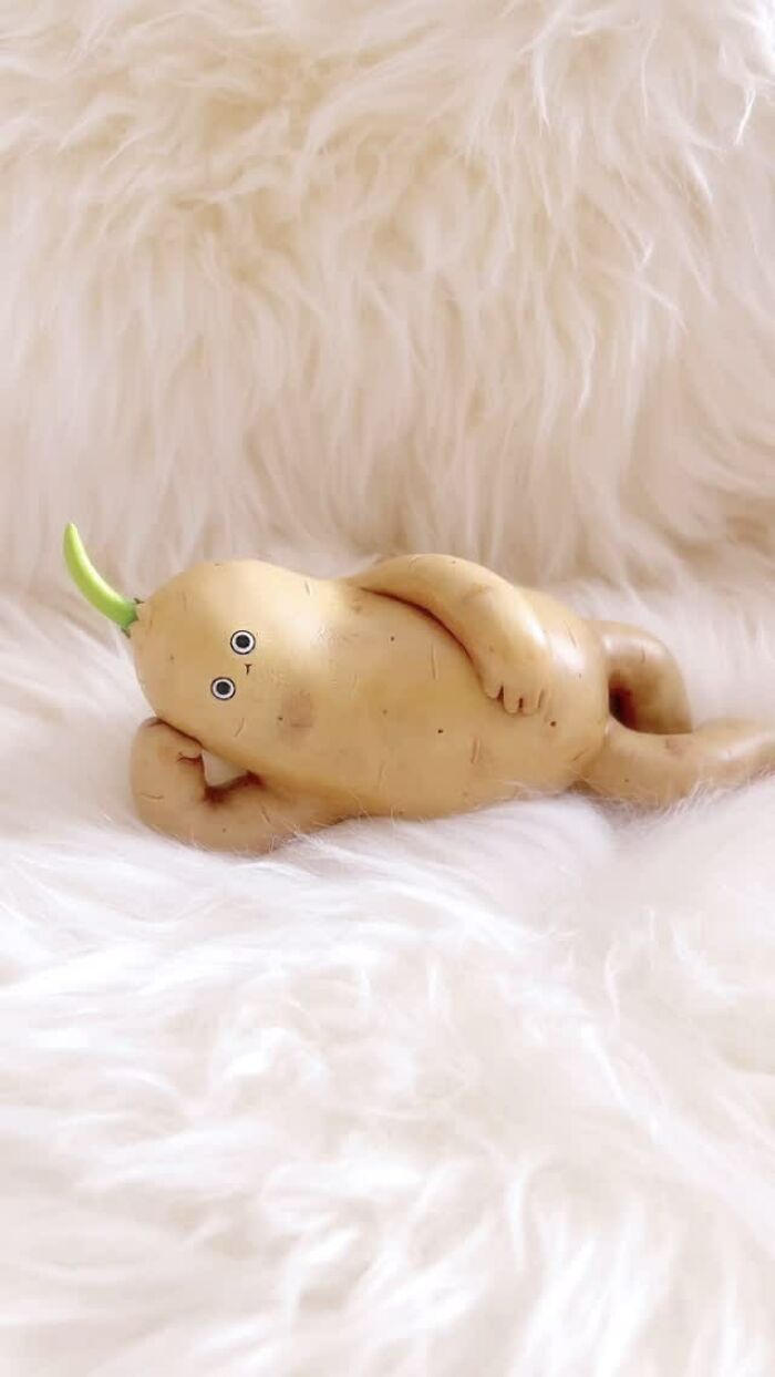 Quirky sculpture of a potato character with arms and googly eyes lying on a soft white furry surface.