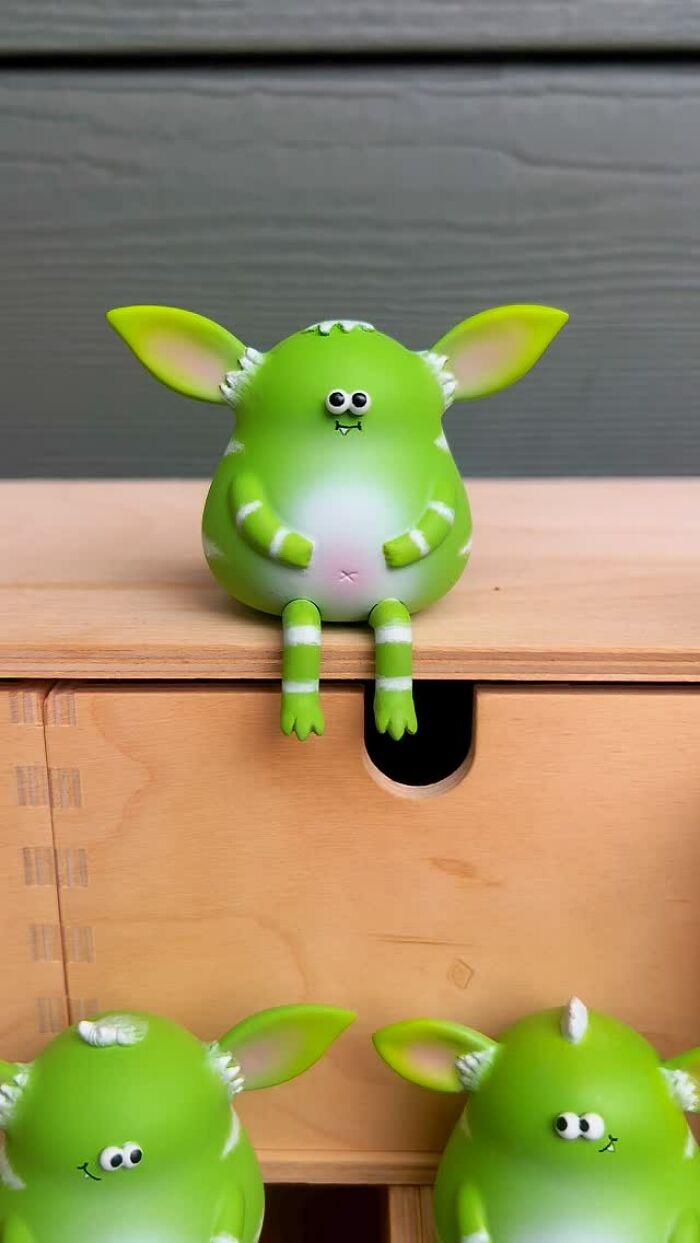 Green quirky sculpture sitting on wooden drawer with playful expression, showcasing artist made quirky sculptures bursting with personality.